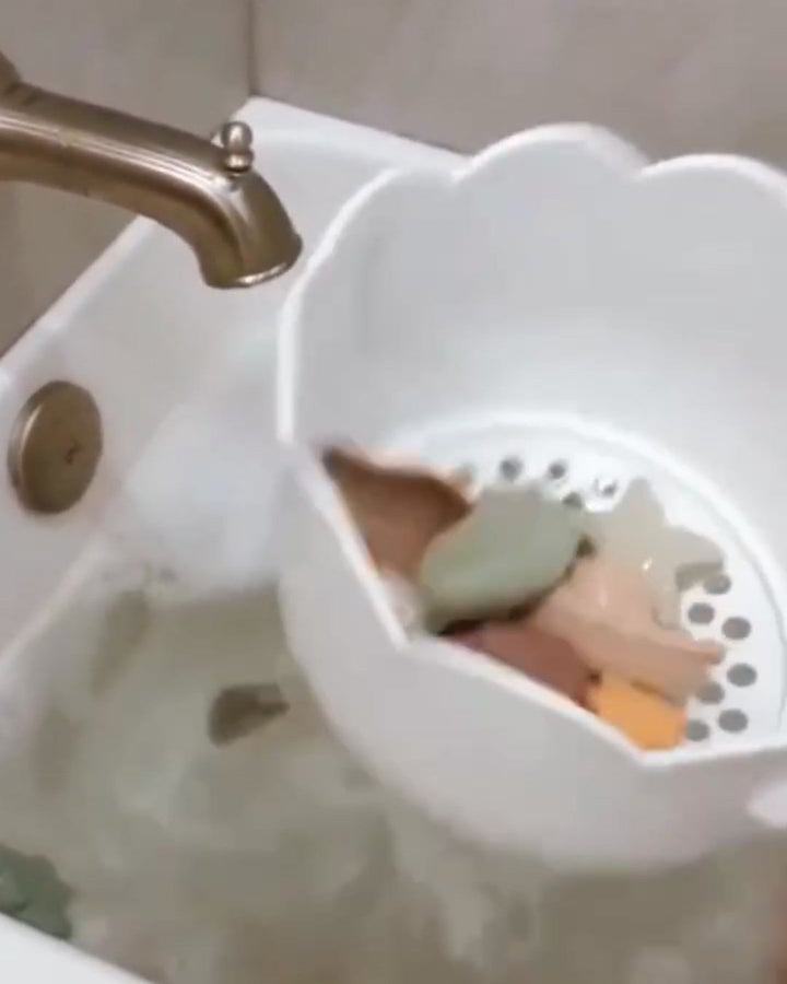 Bath Buddy drum under the tap with toys inside and water running out through the holes in its floor