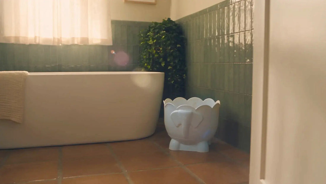 Bath Buddy, a white drum with a scalloped rim standing beside a bathtub in a green-tiled bathroom, in a generated still