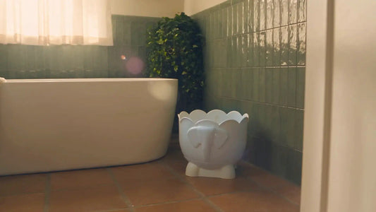 A white elephant-shaped Bath Buddy organizer on the floor beside a freestanding tub in a green-tiled bathroom